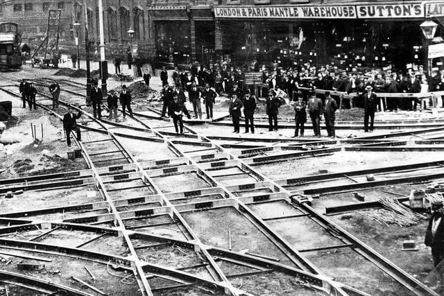Th laying of tramlines at the tramway junction of Boar Lane and Briggate, which took place between September 6 and September 9, 1899. Workmen take a rest from their labour to pose for the camera. A steam tram is seen on the left where tramlines are yet to be laid. on the right is Sutton's London & Paris Mantle Warehouse at no. 73 Boar Lane.