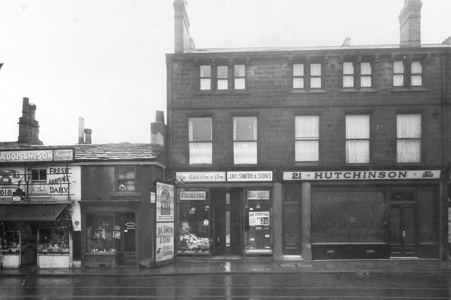 A row of shops on Otley Road in January 1938. On the left is William Addison and son selling fish, fruit and poultry. Painted on wall is a telephone and 'Fresh Arrivals Daily'. To the right is Harry Hanson, saddler, next a florists shop also belonging to William Addison, a sign on the wall with the logo 'Flowers to any part of the World', 'The Mercury Way' with a picture of the God Mercury. Then James Smith, cleaners and dyers, followed by butchers shop owned by Percy H Hutchinson.
