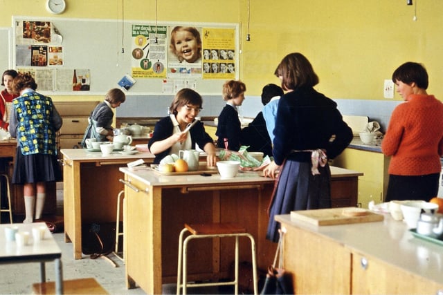 A cookery lesson for female pupils is taking place in the Cookery Room in October 1966. The pupils are part of Form 1A and appear to be preparing a meal which includes a pot of tea, possibly breakfast. A poster on the notice board informs about the importance of dental care.