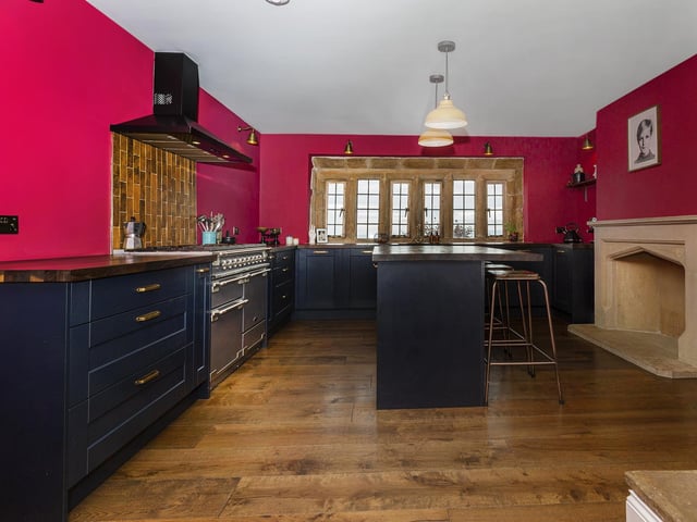 The fitted breakfast kitchen with black oak worktops has a central island and an open stone fireplace. A Rangemaster dual fuel oven with a six-ring gas hob is among integrated appliances that include a fridge freezer and dishwasher.