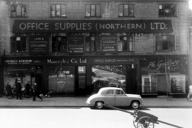 The south side of Park Lane in June 1950. The premises are; number 59, C. Kershaw, nurseryman; number 61, Muscroft & Co. Ltd., wines and spirits; number 63, Office Supplies (Northern) Ltd; number 65, P. Godlove, tailor. A car and a handcart are in front. Pedestrians can be seen, as can a ladder against Godlove's wall.