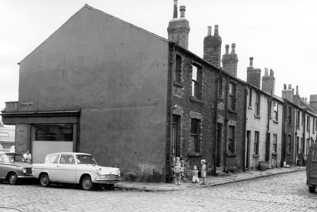 The junction of Selkirk Street and Mount Place in August 1964. On the far left is Dewsbury Road and just visible is shop number 148, domestic furnishers, furniture suppliers. Two cars are parked on Selkirk Street and at the corner of Mount Place six boys sit and stand in the doorway of number 11. On the right can be seen the back-to-back terraced houses of Mount Place.