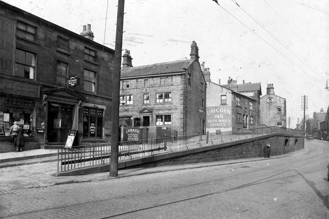 Properties in Stocks Hill, Lower Town Street in September 1933. The three-storey, stone built block on the left houses numbers 145 to 147A. Number 147A, at the left edge is the premises of James Blakey, photographer, and examples of his work are displayed in the window. A woman is holding a small child up to the window to get a better view of the photographs. Moving right, number 147 is a branch of the Leeds Permanent Society.