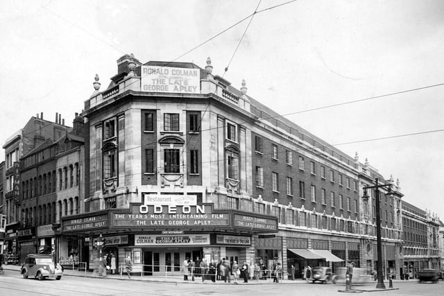 The Odeon Cinema and The Headrow pictured in June 1947. The film showing is 'The late George Apley' and outside there are people meeting, there is a cinema doorman, newspaper sellers and two people talking to a policeman.  On New Briggate number 12 Meesons, 14 Model Makers, 16 Mentels, 18a Chemists and 20 Pitman's College, can be seen. The cinema opened as the Paramount in 1932 and became the Odeon in 1940.