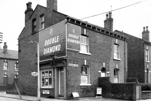 On the left Longwood Terrace can be seen. The off licence, grocers shop is number 35 Joseph Street, business of David Naylor. Painted walls signs advertise 'Double Diamond' beer. Longwood Grove is to the right, number 28 is adjacent to the shop.
