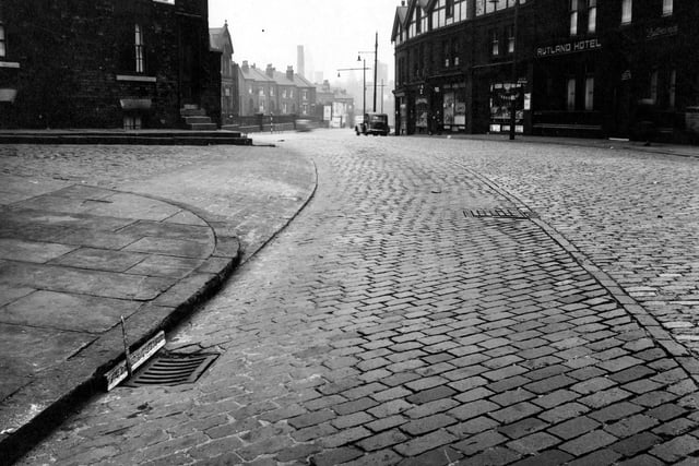 This low level view, looks east down Burley Street towards Park Lane in October 1951. Back Burley Street is on the left. On the right is number 9, The Rutland Hotel, with shops at numbers 1 to 7 beyond. A car is parked near the end. In the bottom left is a drain with a ruler propped in it.
