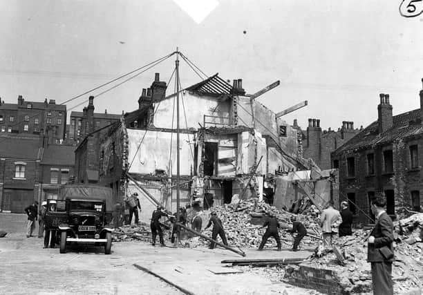 Air raid precaution and rescue personnel simulating a rescue operation. Twelve dummies have been placed in the ruins of the two houses, some of them have been brought out. Here a derrick has been built and is being swung into operation to move heavy debris. The bedford truck has Leeds coat of arms on the door and a sticker on the windscreen.