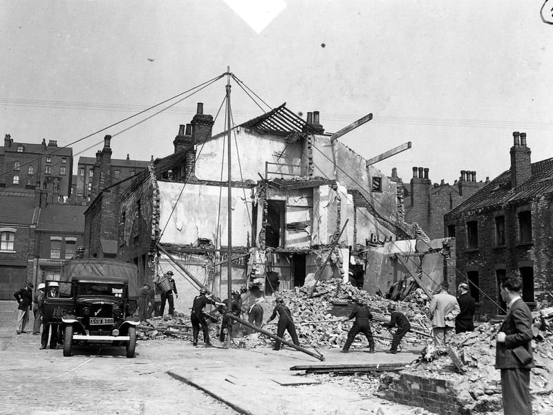 Air raid precaution and rescue personnel simulating a rescue operation. Twelve dummies have been placed in the ruins of the two houses, some of them have been brought out. Here a derrick has been built and is being swung into operation to move heavy debris. The bedford truck has Leeds coat of arms on the door and a sticker on the windscreen.
