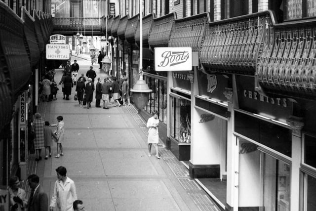 This view looks from the upper balcony across the interior of the Queen's Arcade in the direction of the Lands Lane entrance in August 1966. On the left is a sign for the Handbag Hospital, while a branch of Boots the Chemists is visible on the right.