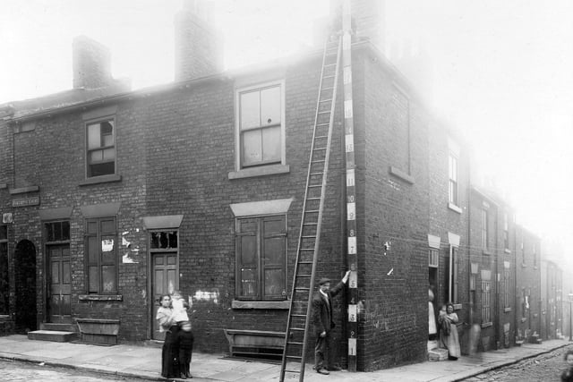 The corner of Edward Street and Little Templar Street in October 1910. Houses in main view are derelict. To the left can be seen entrance to Bakehouse Court. Women and children in the street. Long ladder against end wall and two workmen are holding a measuring pole against the side of the house.