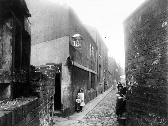 A view looking north along Back Portland Crescent near the junction with St James Place. Number 13 on the left of the narrow cobbled street appears to have a shop entrance. Wooden shutters are on the lower window. Children and a metal bucket are visible. Washing can be seen hanging up. The area is now the site of Civic Hall. Pictured in September 1913.