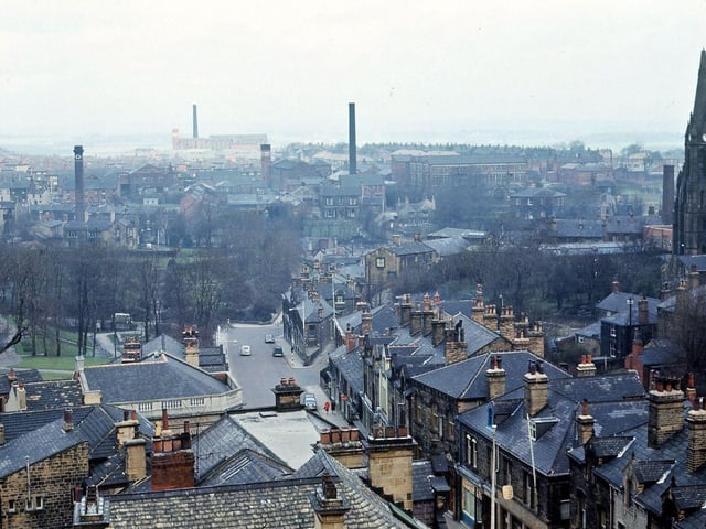Morley Town Hall tower looking towards the north down Queen Street. The roofs of buildings on both sides of Queen Street are shown in the foreground. St. Mary's-in-the-Wood Church can be seen on the right, houses in Scatcherd Park Avenue are in the middle distance and three large mills, Victoria, Springfield and Prospect, dominate the background. Pictured in April 1965.
