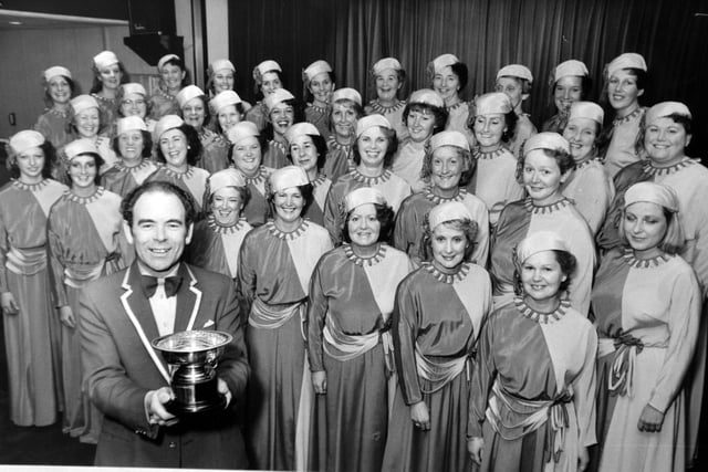 Women with plenty to smile about are members of the Leeds-based White Rosettes Ladies' Barbershop Chorus in October 1983. They won a first-prize at Exeter in the championship organised by the Ladies Association of Babershop Singers. Pictured is the chorus with musical director Clive Landley and the championship rose bowl.