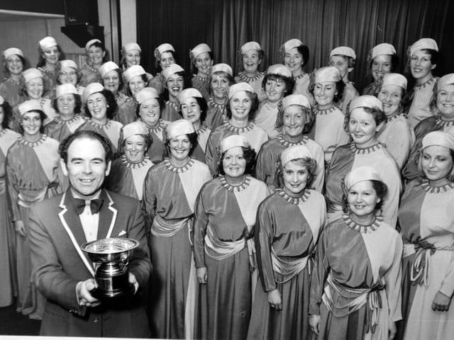 Women with plenty to smile about are members of the Leeds-based White Rosettes Ladies' Barbershop Chorus in October 1983. They won a first-prize at Exeter in the championship organised by the Ladies Association of Babershop Singers. Pictured is the chorus with musical director Clive Landley and the championship rose bowl.