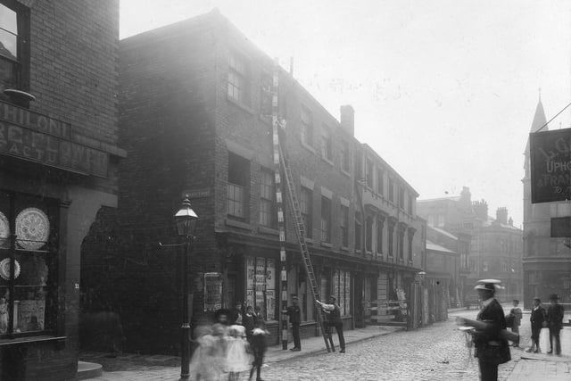 A view looking up Wade Lane with entrance to St. John's Court on the left. Workmen with measuring pole can be seen against side of building. A group of children stand in road.
