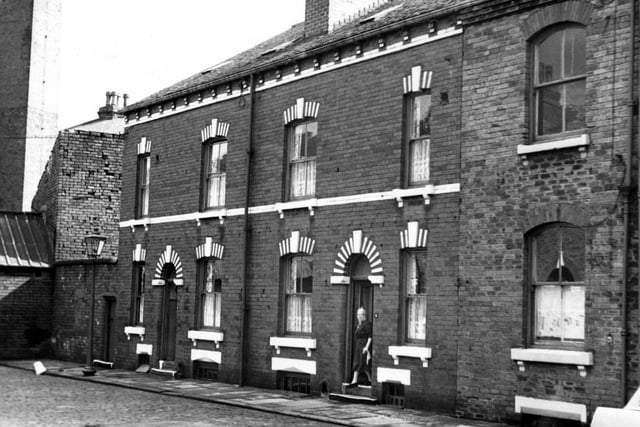 Oakfield Place, on the left is a wall which separates the street from the factory premises. This business was the Roscoe Clothing Company. Three houses are in view, number 6 is on the left, 4 has a woman in the doorway. The empty house on the right is number 2. Pictured in August 1967.