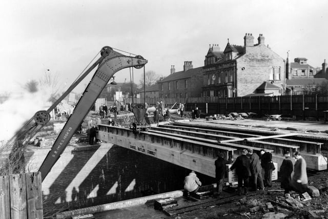 Improvement or reconstruction work being carried out on Cross Gates Bridge in January 1955. A crane can be seen lifting girders into position whilst workmen stabilise them at each end. A crowd has gathered to watch.