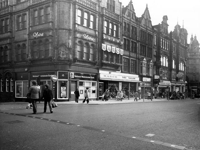 Vicar Lane showing the junction with Sidney Street on the left. Shops include National Westminster Bank, March the Tailor, Photomarket and Bargin Records. Several shoppers are in view including a queue of people waiting at a bus stop on the right. The junction with Ludgate Hill and Kirkgate Market Buildings can be seen on the far right. Pictured in January 1980.