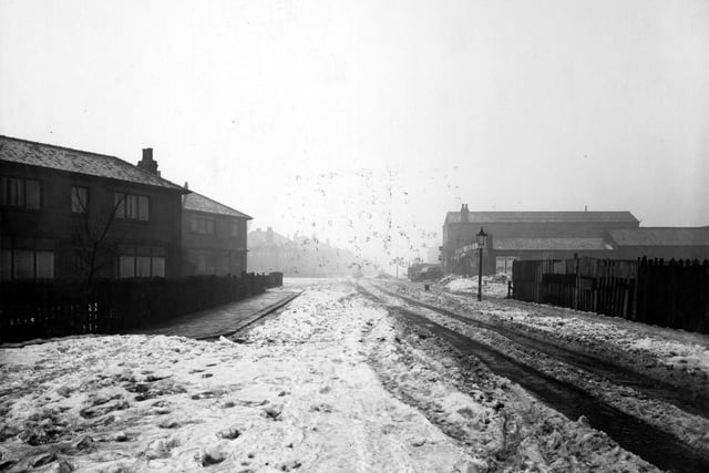 A snow covered Barkly Road  in February 1940. On the right a length of fencing and a gas lamp. Behind the lamp is Universal Garage with car in front.