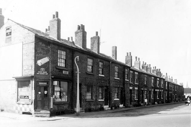 On the left of the image and in the foreground is New Princess Street with number 1 visible at the corner. This is a grocery advertising products including Zebrite polish, Tizer, Lyons coffee and tea and Senior Service cigarettes. On the right of the image is a row of back-to-back terraced houses numbers 1 to 19 Clowes Street.