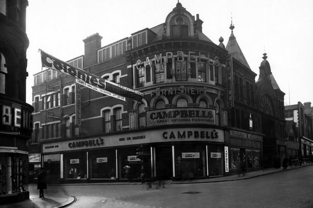 The south qwest side of The Headrow at the junction with Lands Lane in February 1944. On the far left is number 69 Benefit Footwear Ltd. Over the road is number 73 Campbell and Co. furnishers, 75 H.G. Shipham Ltd. hosiers, next is Victoria Arcade. A banner for "Colonies Exhibition" is hung across the road. A women in uniform stands on the left.