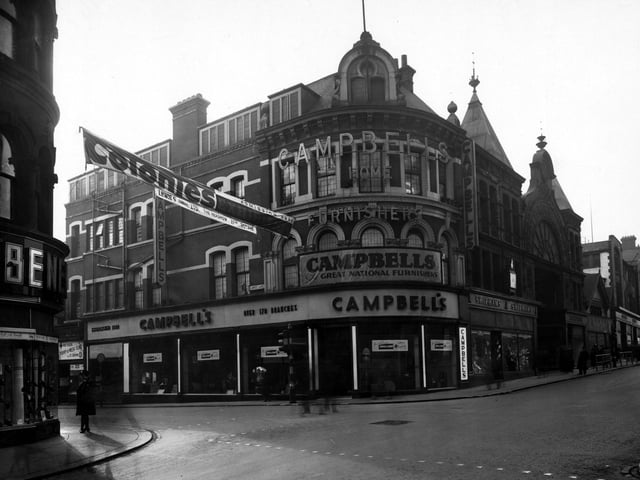 The south qwest side of The Headrow at the junction with Lands Lane in February 1944. On the far left is number 69 Benefit Footwear Ltd. Over the road is number 73 Campbell and Co. furnishers, 75 H.G. Shipham Ltd. hosiers, next is Victoria Arcade. A banner for "Colonies Exhibition" is hung across the road. A women in uniform stands on the left.