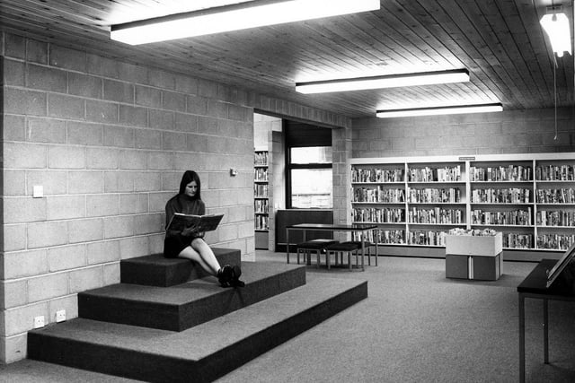 A member of staff poses with a book on a carpeted seating area for children in the new Calverley County Library. This arrangement would be suitable for a small audience of young library users at story Times. 'Stories for Young People' are arranged along the walls and there is a table with 4 stools for homework studies. A book box contains picture books for very young children and toddlers. Calverley County Library opened on September 25, 1973. It was previously located in the Mechanics Institute in Thornhill Street. This purpose-built library is also situated in Thornhill Street.