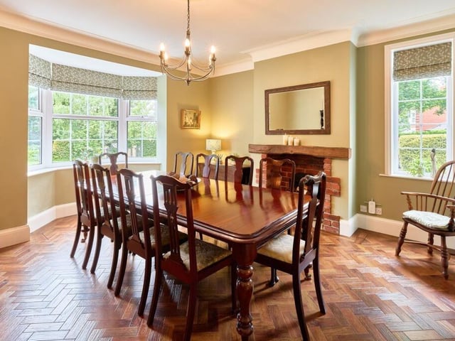 The dining room has tall ceilings, a grand chandelier, Karndean parquet flooring and a brick fireplace with a deep oak mantel.