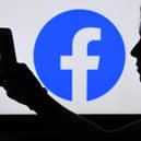 In this photo illustration, a person looks at a smart phone with a Facebook App logo displayed on the background, on August 17, 2021, in Arlington, Virginia. (Photo by OLIVIER DOULIERY / AFP) (Photo by OLIVIER DOULIERY/AFP via Getty Images)