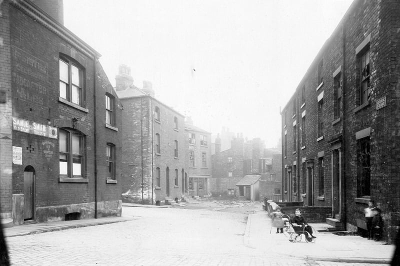 Leeming Square, looking east from Cankerwell Lane in August 1913. Advertising signs on side wall for Samuel Smiths' and Bass beers. There is a mixture of house style and size, many ready for demolition. This was to provide an extension to Calverley Street. On the right, a group of children, one sat in a push chair, holding a hoop.