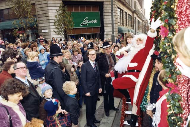 Crowds of people line The Headrow near Dortmund Square and the corner of Lewis's department store. The decorated float depicting a western steam engine can be glimpsed right. It was Lewis's entry in the 7th Lord Mayor's Parade and the overall winner. Santa waves to the crowds and behind him is a young lady dressed very regally later seen riding on the float. The gentleman seen centrally with spectacles is the General Manager of Lewis's, Steven Arundel. It was a blustery, showery day and many onlookers are wearing warm coats and hats. The view looks east towards Eastgate.