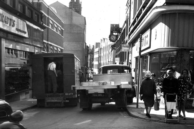 A view looking along Trinity Street from the junction with Commercial Street in June 1966. Barratt's shoe shop is on the left, in the same position it still occupies today (2011). The narrow street, which is proving to be difficult for large vehicles to access, at the time led all the way down to Boar Lane, coming out by Holy Trinity Church whose spire can be seen on the skylin