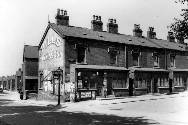 The corner of Seaforth Avenue and Foundry Lane in June 1939 showing a shop with advertisements for Parkinsons Pills, Players Navy Cut, a street lamp, people in the far distance and a woman with a basket. Back-to-back houses.