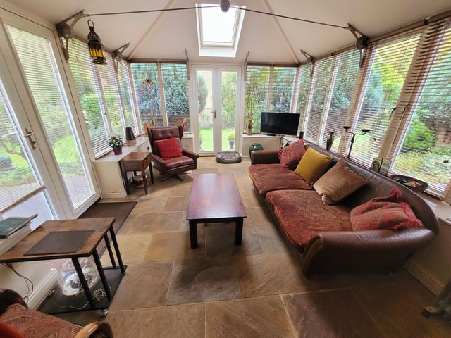 This conservatory has all-round views of the lawned and leafy garden with doors leading outside.