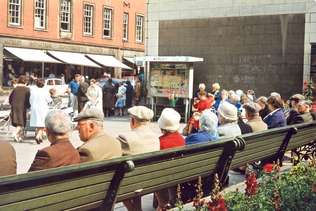 Public seating in Queen Street in front of the gardens of Windsor House at the junction of Albion Street and Queen Street in July 1965. This area of open space was created when the former gas and/or electricity showroom building at the side of the Town Hall buildings was demolished in the early 1960s. The side of the Town Hall buildings has been exposed and an illuminated street plan of Morley showing 'You are here' placed at its side. The area remained clear until 1972 when the shops and banks of the Windsor Court shopping precinct came to the edge of Queen Street again.
