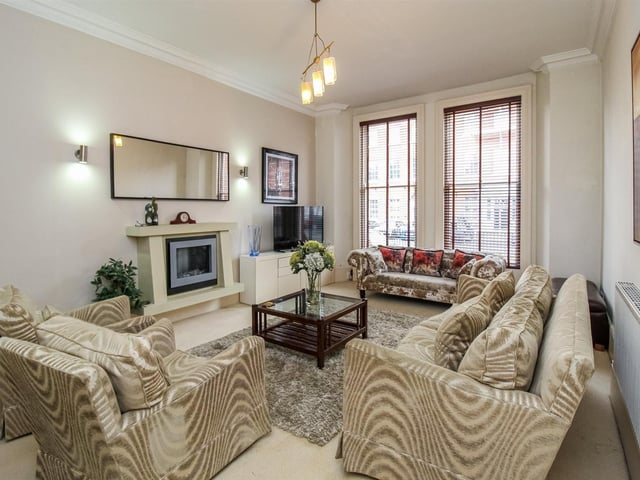 The stunning sitting room with sash windows that have original timber surrounds, and a wall-mounted feature electric fireplace.