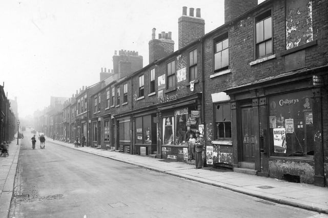 Byron Street taken from south-west corner of the junction with Regent Street. Centre right is Mac-Sky Stores, owned by Sam Macofsky. Two men and a boy pose in the entrance to shop. Row is a mixture of houses and shops, mainly derelict. Photo is facing uphill towards North Street. The roof of the Polish -Jewish synagogue is just visible. Pictured in August 1935.