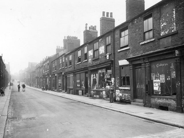 Byron Street taken from south-west corner of the junction with Regent Street. Centre right is Mac-Sky Stores, owned by Sam Macofsky. Two men and a boy pose in the entrance to shop. Row is a mixture of houses and shops, mainly derelict. Photo is facing uphill towards North Street. The roof of the Polish -Jewish synagogue is just visible. Pictured in August 1935.