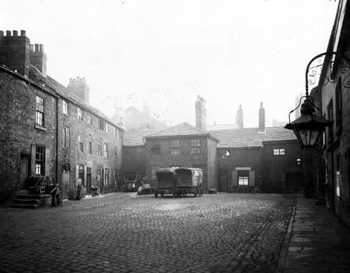 Yard at the rear of Marsh Lane pictured in February 1934. In centre view are two covered carts. A man is sitting in an upstairs window. To the right is an ornate gas lamp suspended from a wrought iron wall bracket.