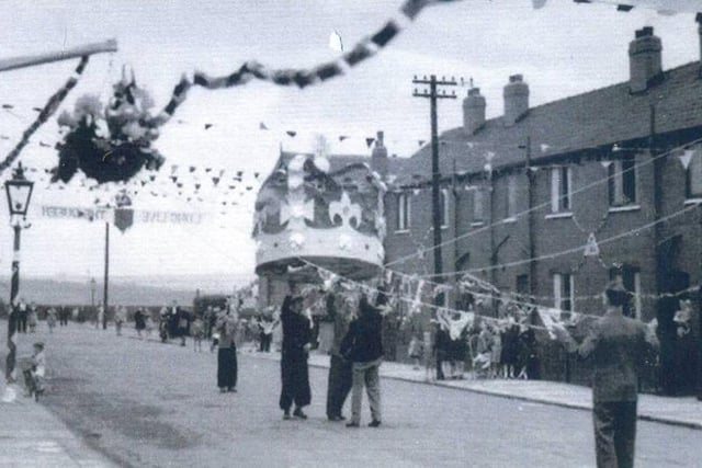 A large model of a crown being pulled into place during preparations for the celebrations for the coronation. The view looks south-east to the junction with Copperfield View, and over fields towards Pontefract Lane. The lettering strung across the street probably reads "God Save The Queen".