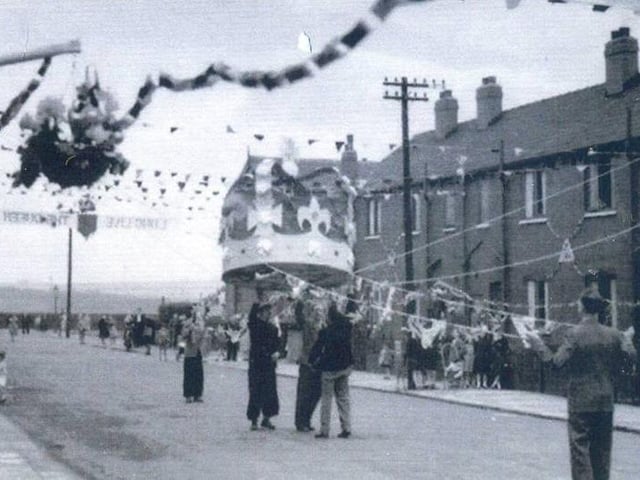 A large model of a crown being pulled into place during preparations for the celebrations for the coronation. The view looks south-east to the junction with Copperfield View, and over fields towards Pontefract Lane. The lettering strung across the street probably reads "God Save The Queen".
