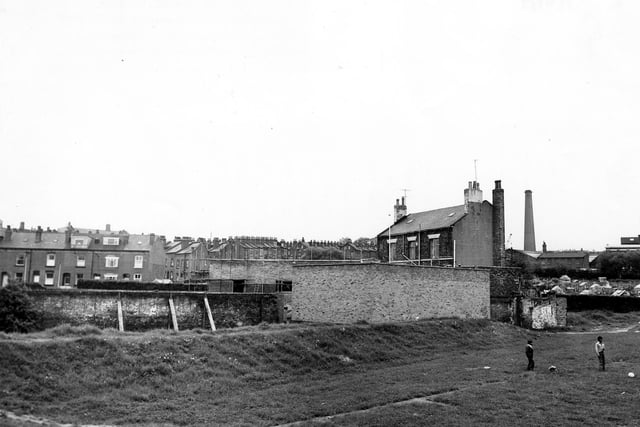 The Conservative Club on Dewsbury Road, seen from playing fields to the north. Scaffolding covers part of the buildings. Rows of terraced housing can be seen in the background, with Crossland Terrace being prominent. On the right are allotments. Two boys play on the playing field in the foreground. Pictured in June 1979.