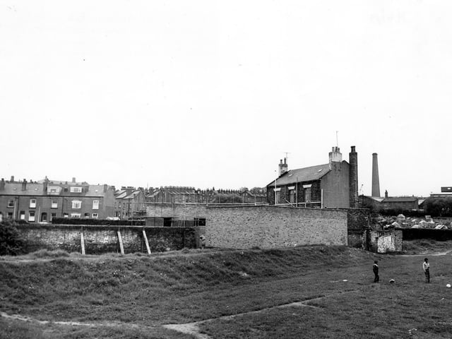 The Conservative Club on Dewsbury Road, seen from playing fields to the north. Scaffolding covers part of the buildings. Rows of terraced housing can be seen in the background, with Crossland Terrace being prominent. On the right are allotments. Two boys play on the playing field in the foreground. Pictured in June 1979.