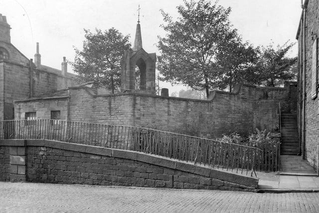 A view of the cobbled street of Stocks Hill, showing a sloping pavement with railings. What could possibly be the former bell tower of St. Margaret's church is behind a high stone wall. St. Margaret's was behind the Old Unicorn Inn. Pictured in September 1933.
