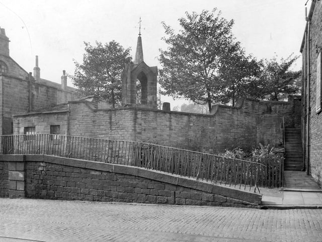 A view of the cobbled street of Stocks Hill, showing a sloping pavement with railings. What could possibly be the former bell tower of St. Margaret's church is behind a high stone wall. St. Margaret's was behind the Old Unicorn Inn. Pictured in September 1933.