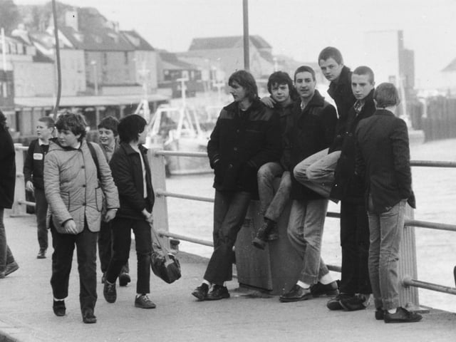 Young unemployed of Whitby while away time as schoolchildren pass in March 1982.