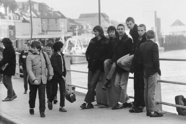 Young unemployed of Whitby while away time as schoolchildren pass in March 1982.