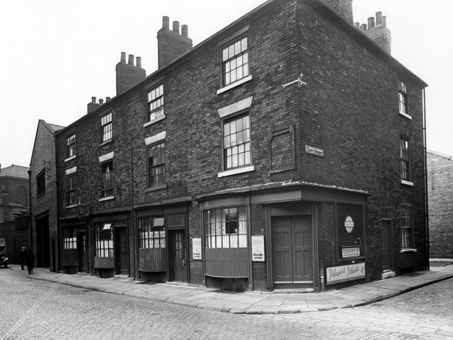 Croft buildings on Water Lane in August 1950. Three storey brick buildings with bowed windows. Corner of Croft Street visible. Corner building possibly shop owned by Mrs Jones advertising Players and Craven "A" cigarettes.