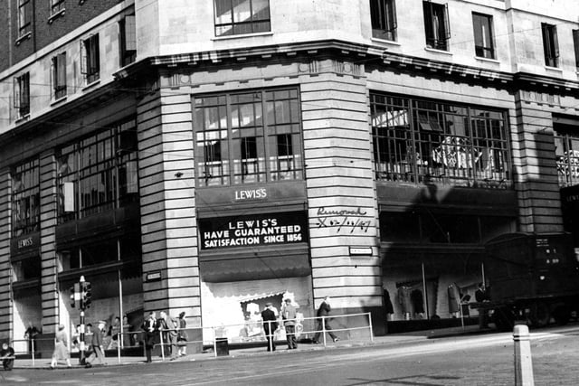Shows Lewis's department store on the corner of The Headrow and New Briggate in August 1947. 'Satisfaction Guaranteed' signs outside.