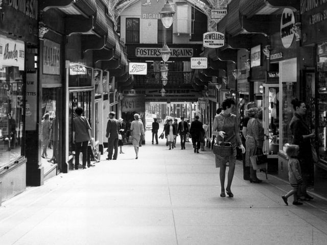 A view of the Queen's Arcade looking from Lands Lane in the direction of Briggate in July 1967. It was built in 1889 on the site of the Rose and Crown public house, also known as Bink's Hotel. Two years before this photograph was taken, in 1965, Queen's Arcade sold for £830,000. Small businesses are situated at first floor level where there is a balcony. Shops at street level include Brown's Toy Shop, established in 1889, at number 20; Boots the Chemist and several ladies hairdressers.